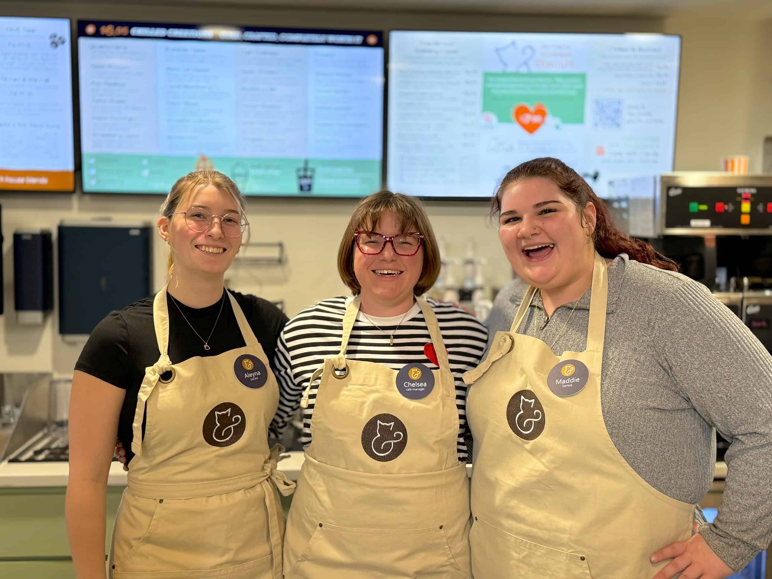 Three smiling staff members in aprons at Biscuits & Beans Cat Café, promoting job openings.